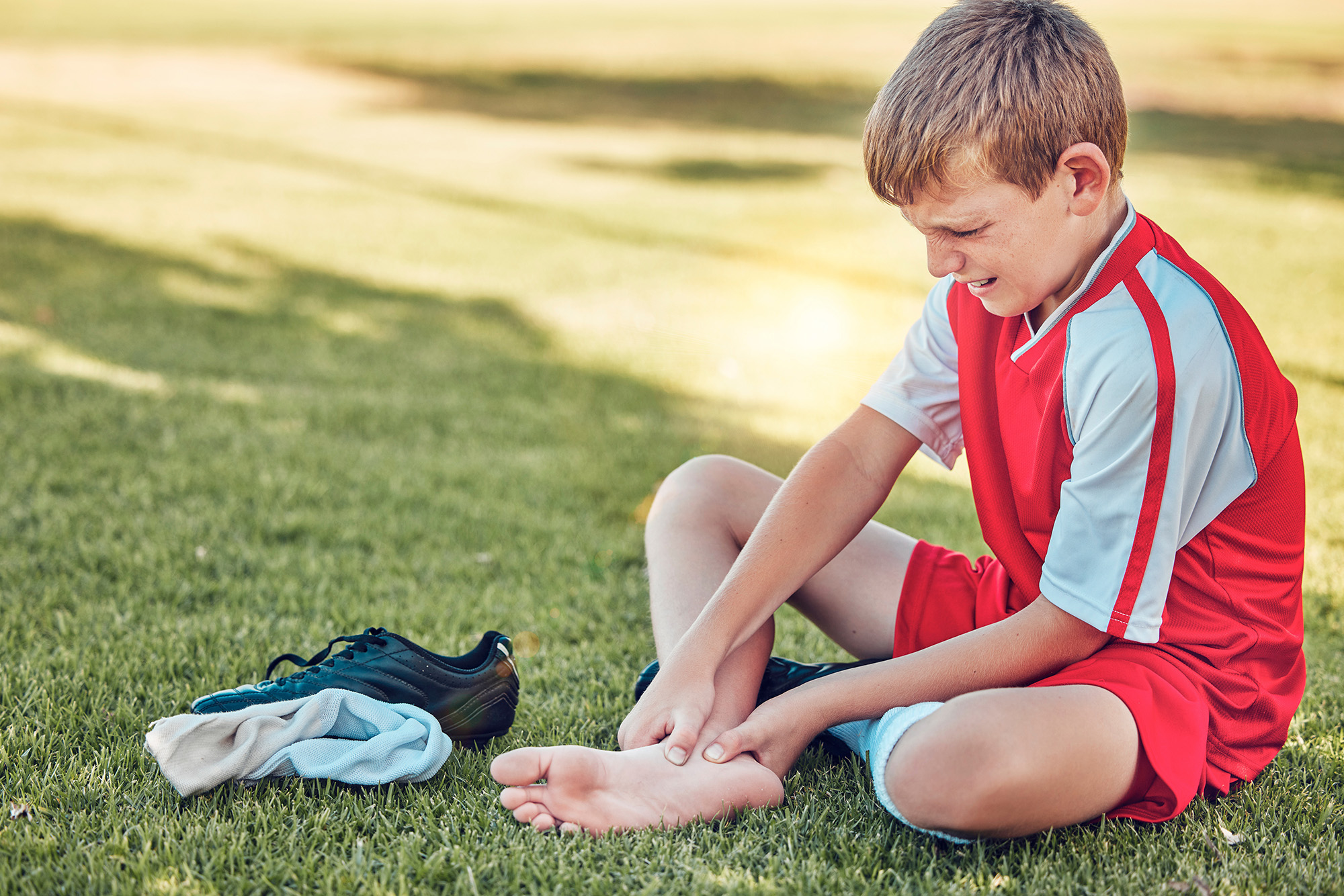 https://elements.envato.com/soccer-injury-and-pain-of-child-foot-on-field-cry--EFYSVTZ ALT TEXT: Young boy sitting on the grass holding his foot in pain after playing soccer, showing signs of foot discomfort or injury
